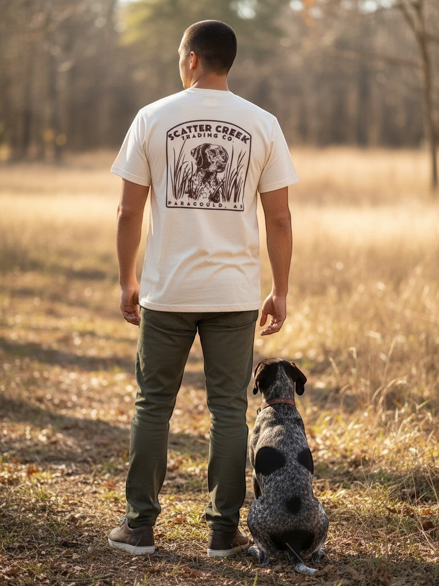 Man wearing a Scatter Creek Trading Co cream heavyweight cotton t-shirt with a pointer dog graphic in a field